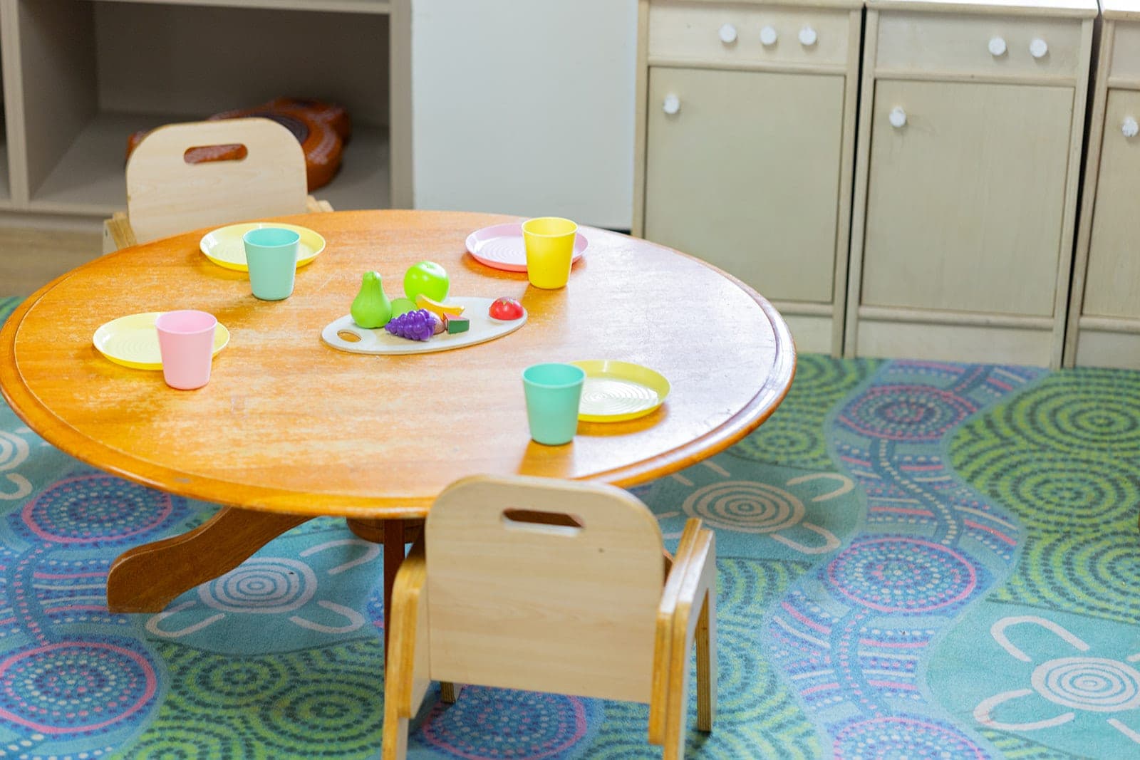 Pastel cups and plates set out for pretend play on a round timber table