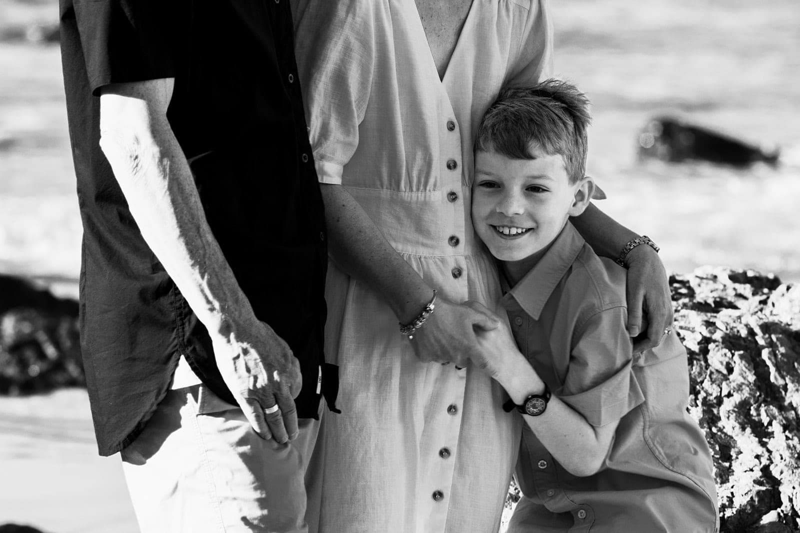 Black and white photo of a boy hugging his mum, grinning at the camera