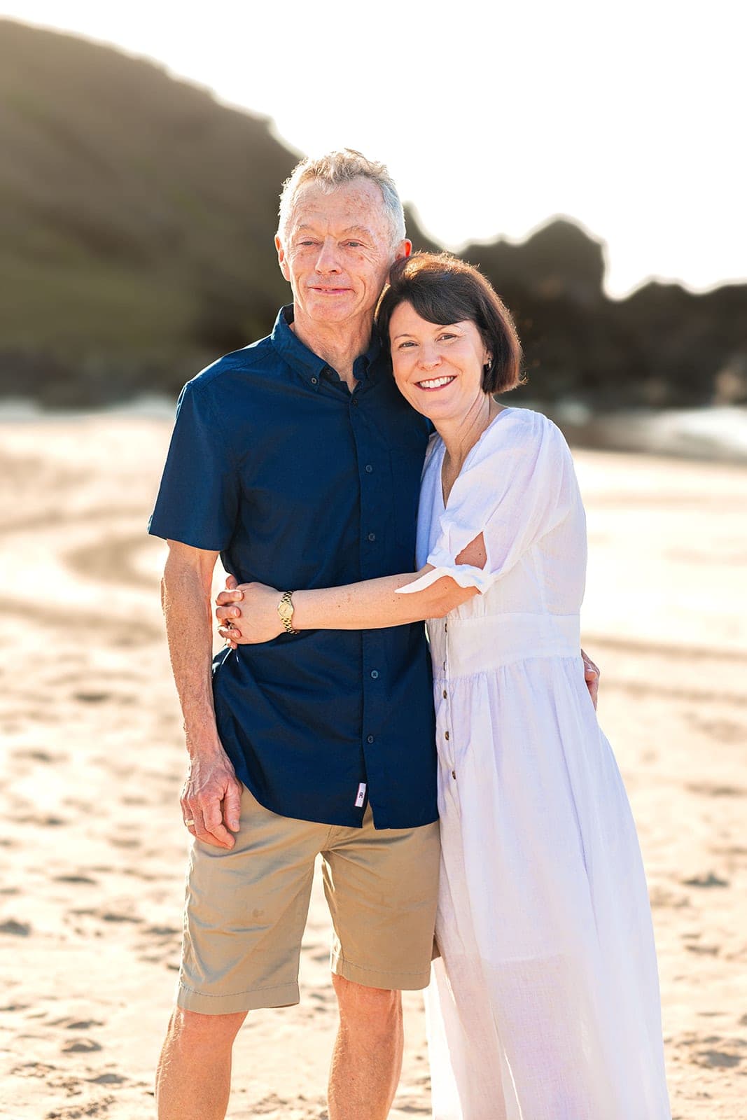 Wife hugging her husband from the side on the sand