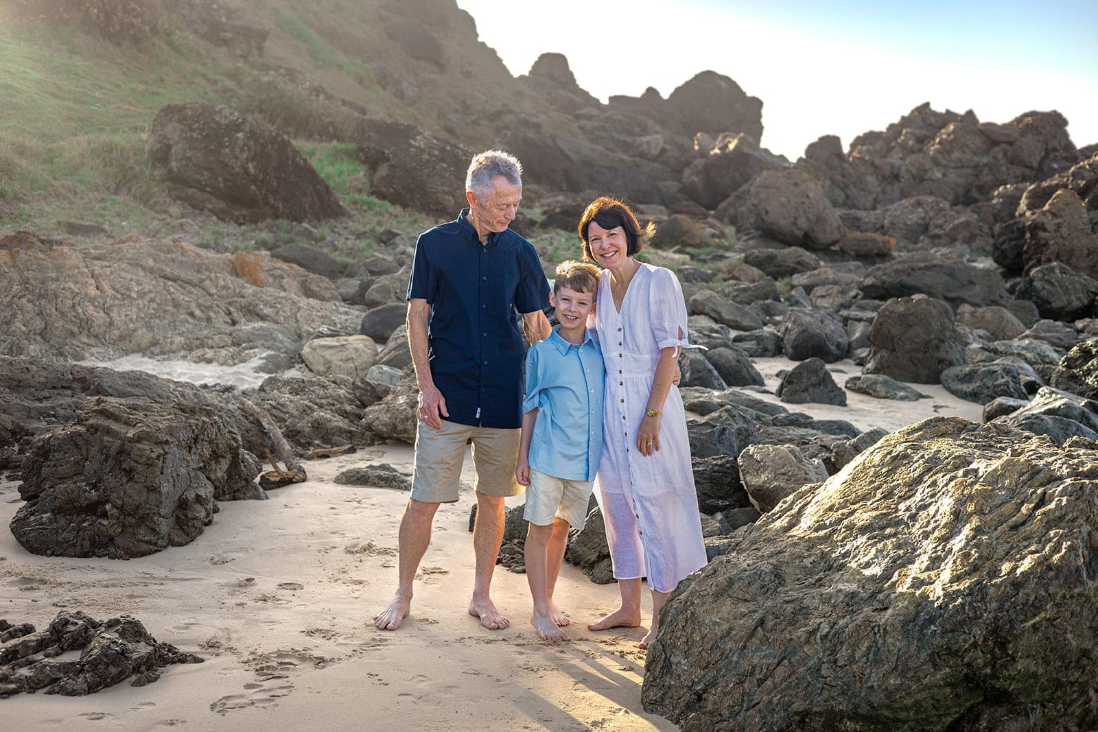 Family standing among sunlit rocks on the beach