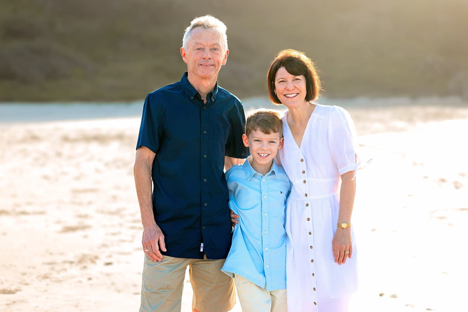 Mum, dad and son smiling close together on a bright beach