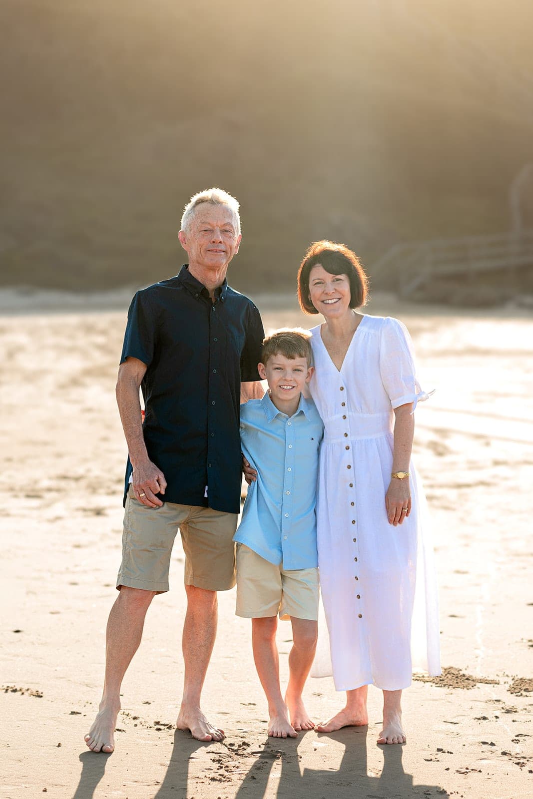 Family of three in soft golden light below the headland