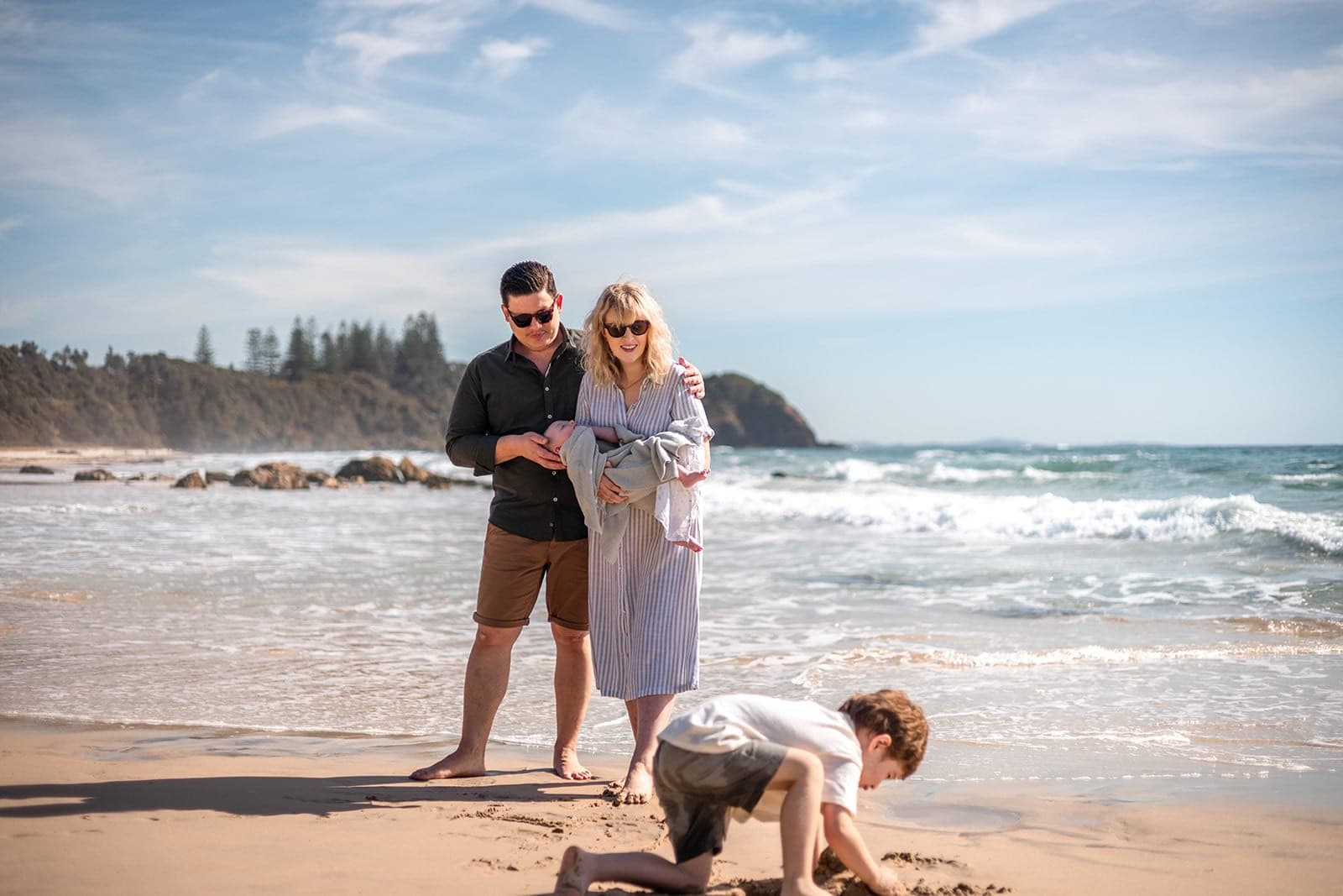 Parents watching their son dig in the sand on a sunny beach