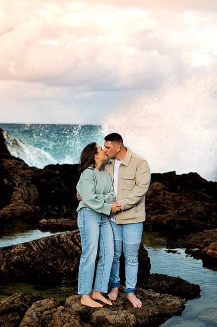 Couple kissing on the rocks as a wave crashes behind them
