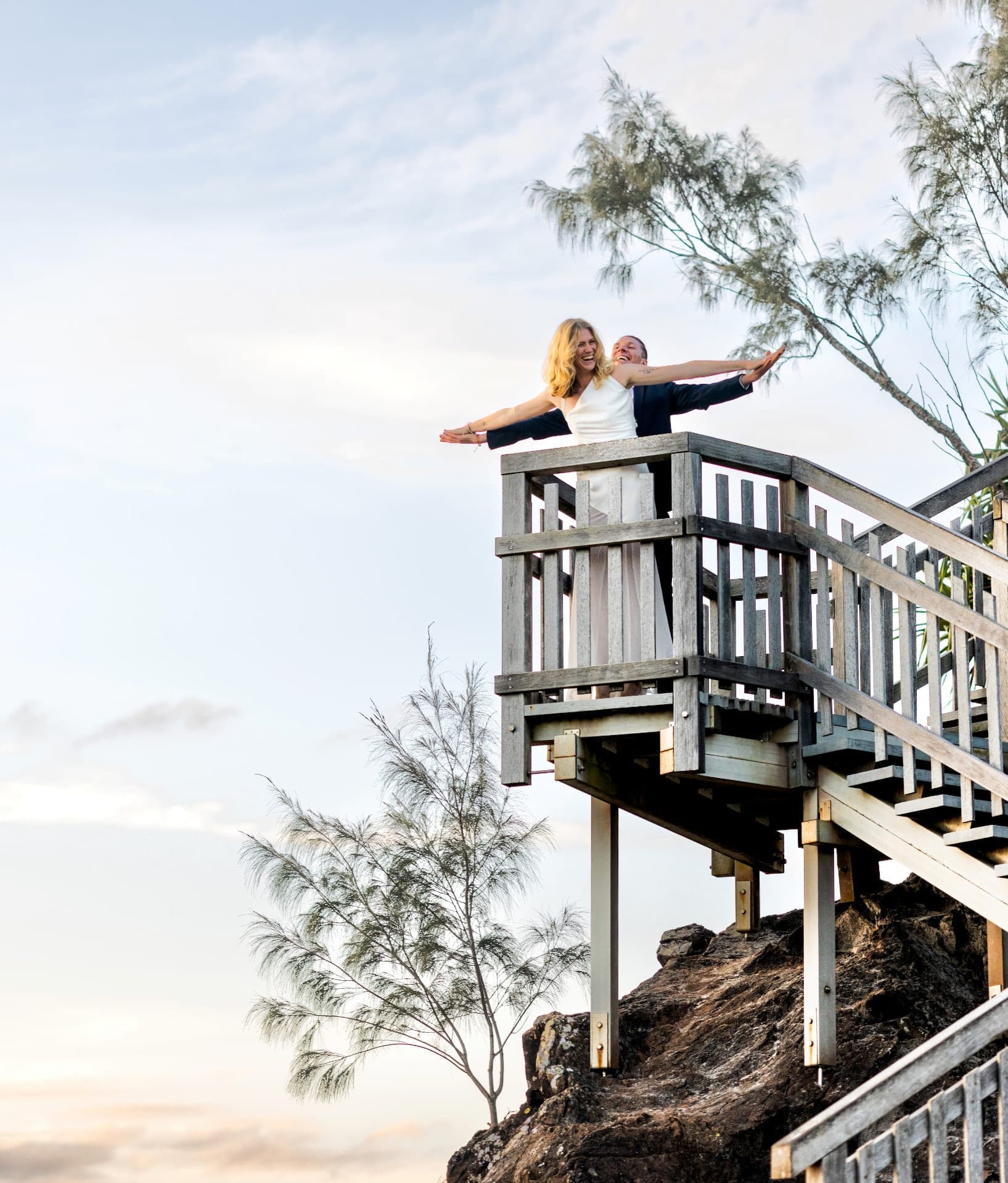 Chloe and JoJo arms outstretched on a coastal lookout against a pale sky