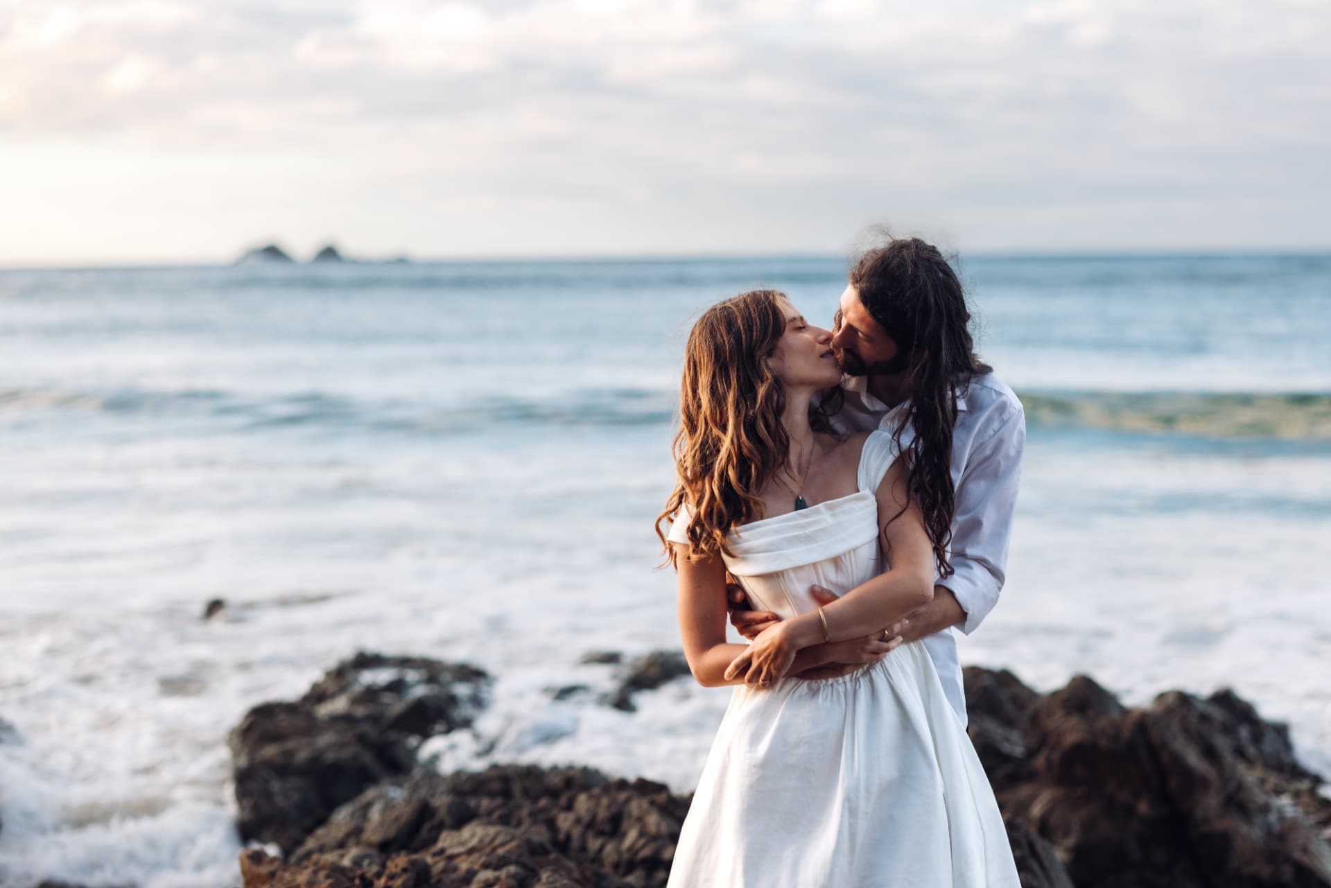 Bride and groom sharing a kiss on the rocks above the surf