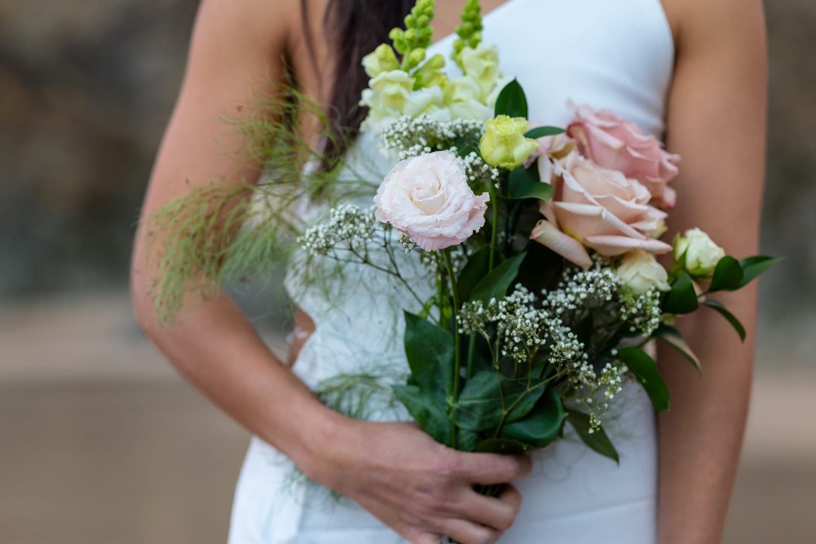 Close-up of a soft pink and white bouquet held against a white dress