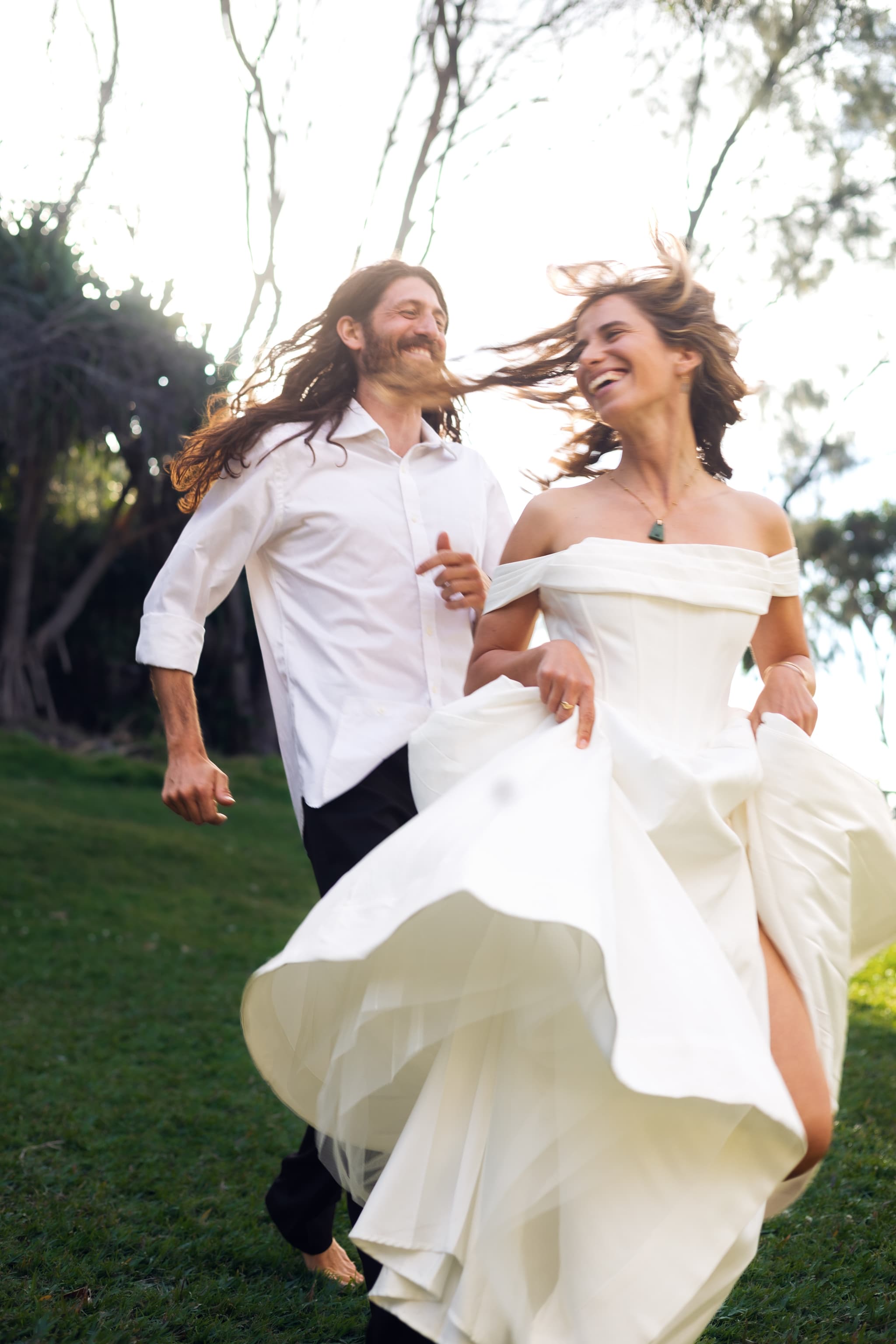 Bride and groom running across the grass, laughing, her dress flying
