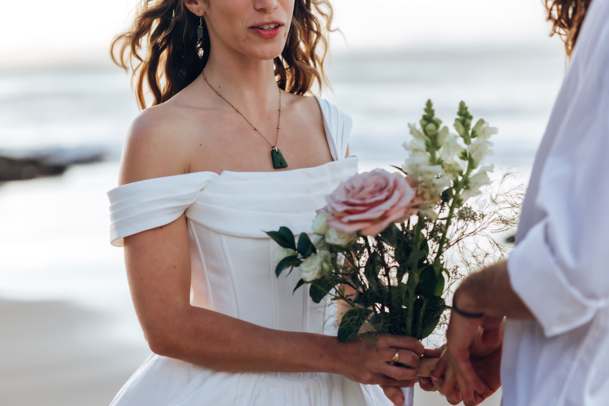 Bride holding a soft pink rose bouquet while saying her vows on the beach