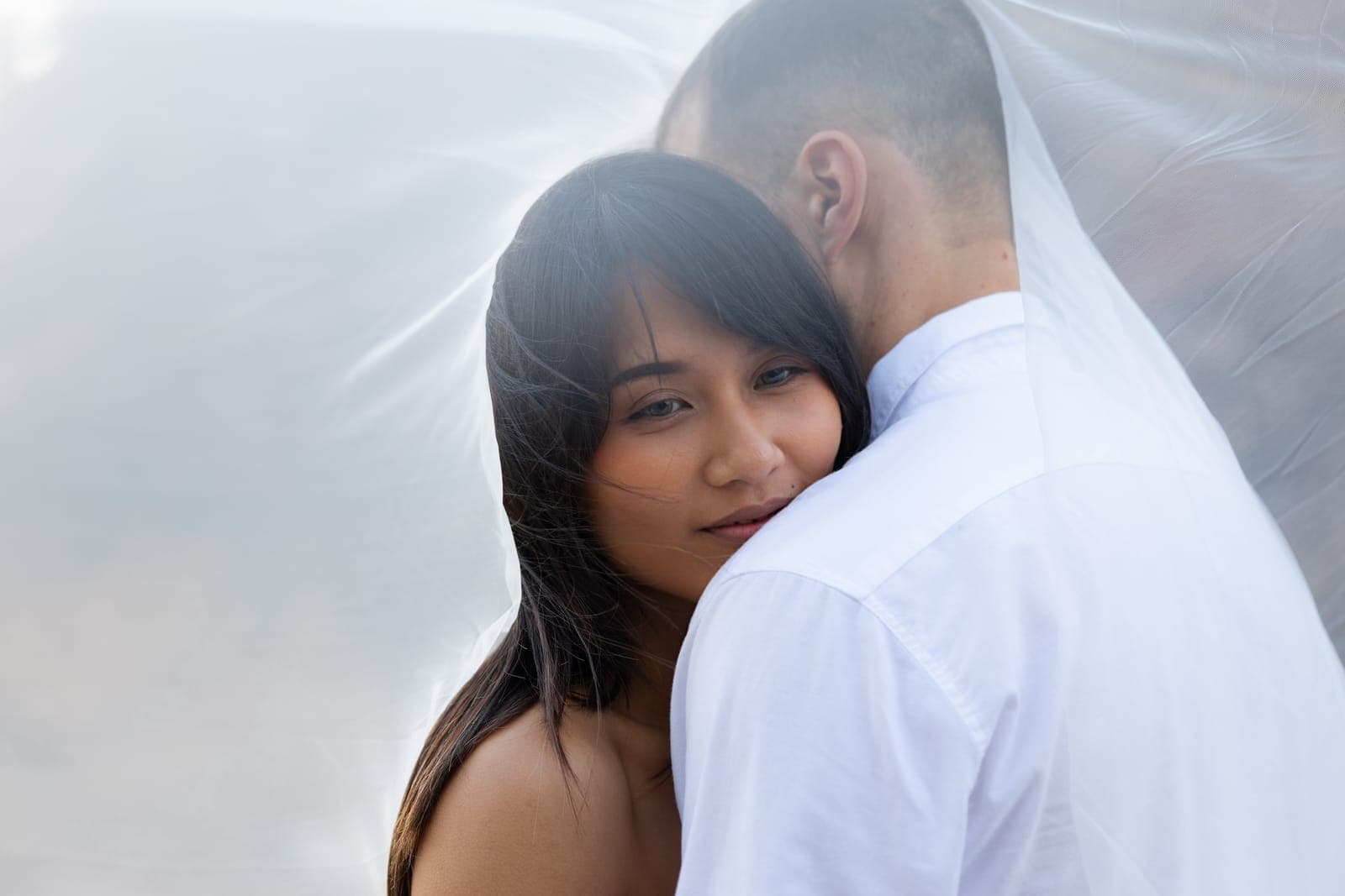 Bride resting her face on the groom's shoulder beneath a flowing veil