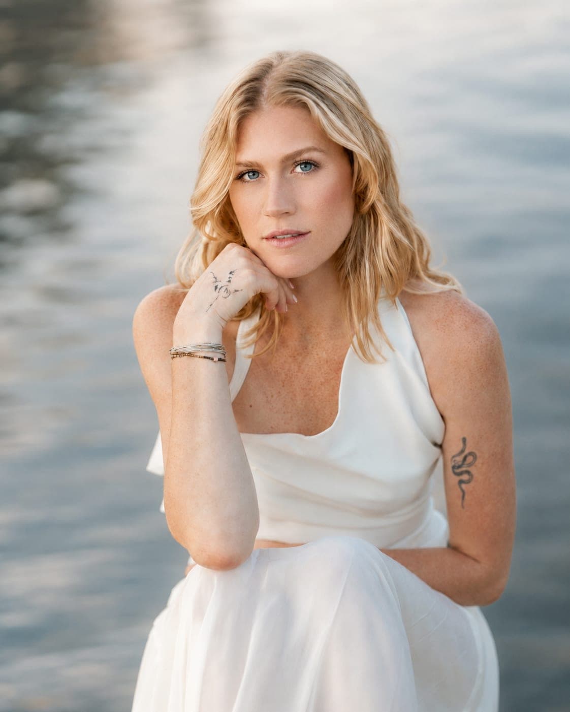 Bride in a white halter gown seated by the water in soft golden light