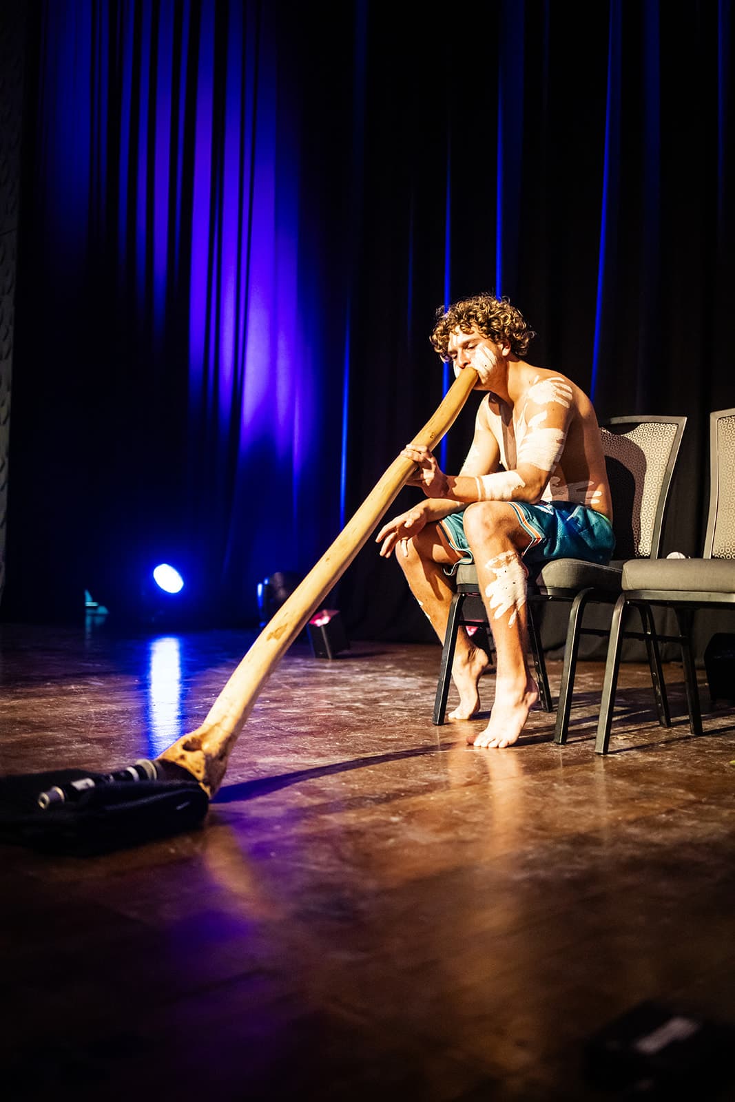 A performer playing the didgeridoo on stage under blue light