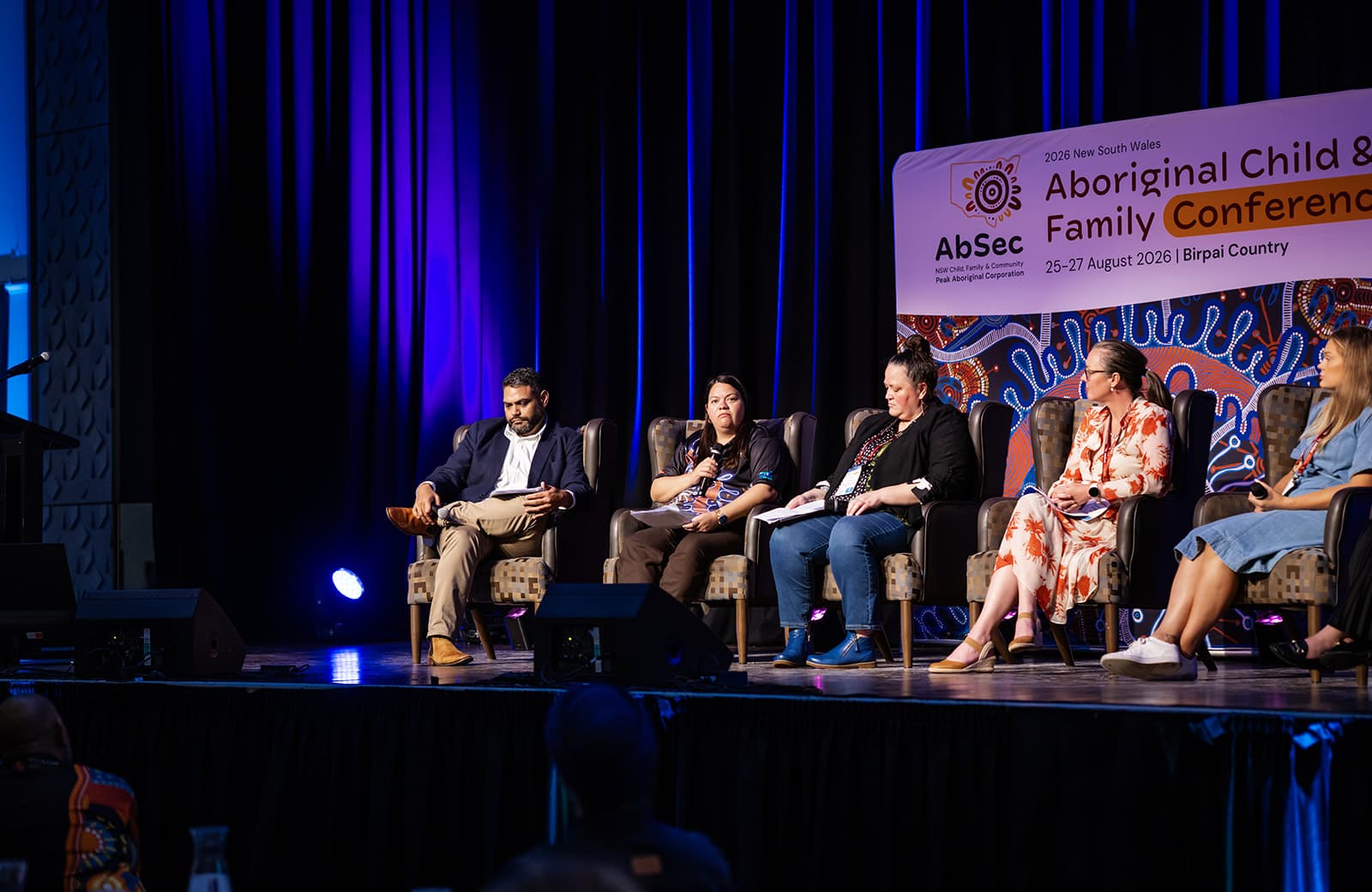 Wide view of a five-person panel on the AbSec conference stage