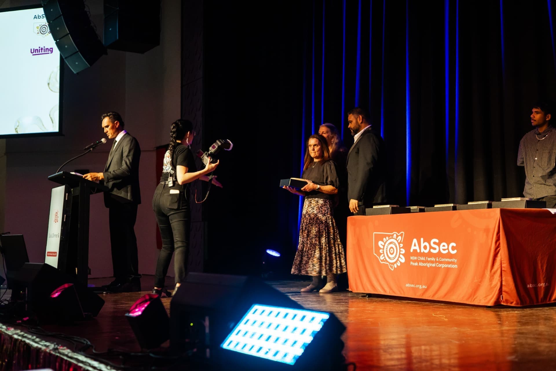 Awards presentation on stage in front of an AbSec banner