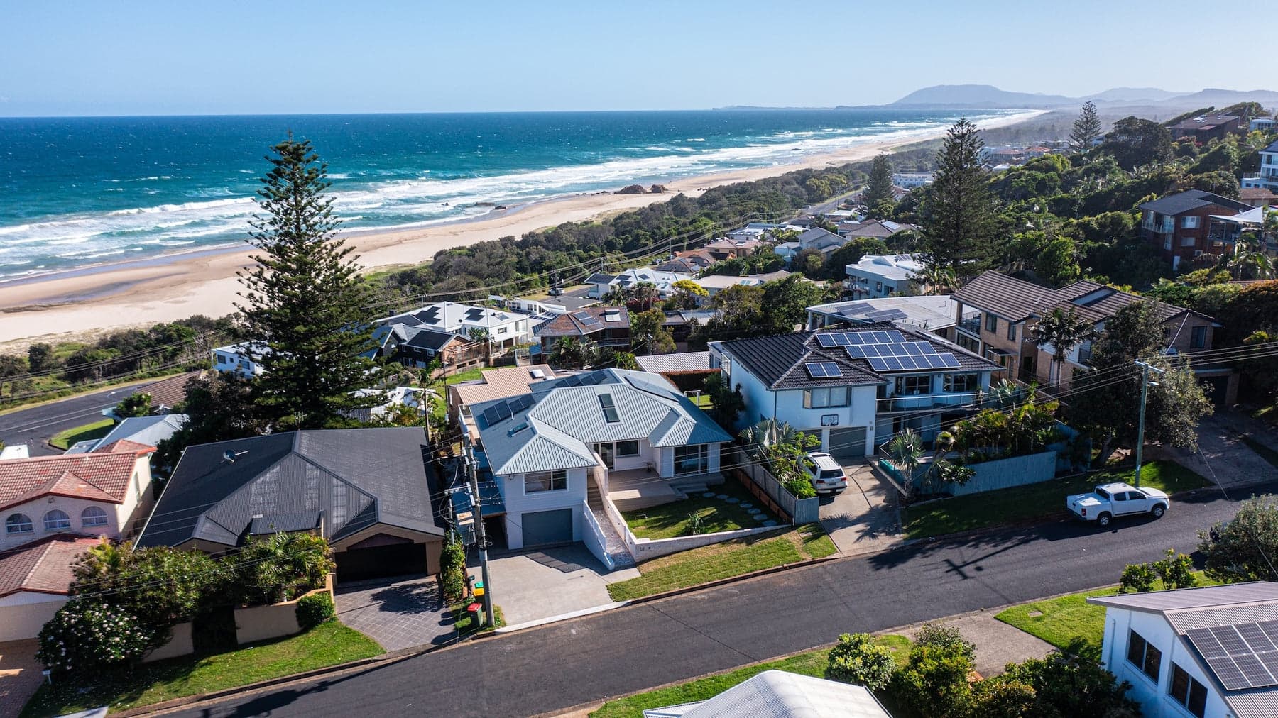 Aerial of a renovated home on a street above a surf beach