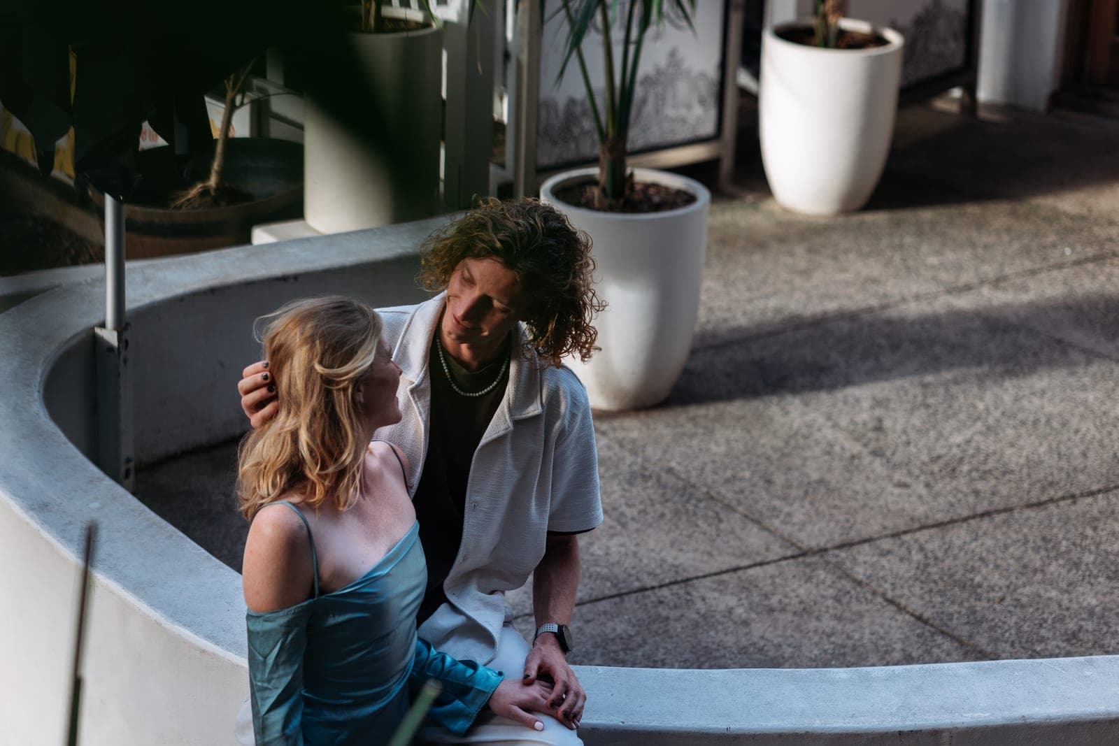 JoJo brushing Chloe's hair back as they sit on a curved white ledge