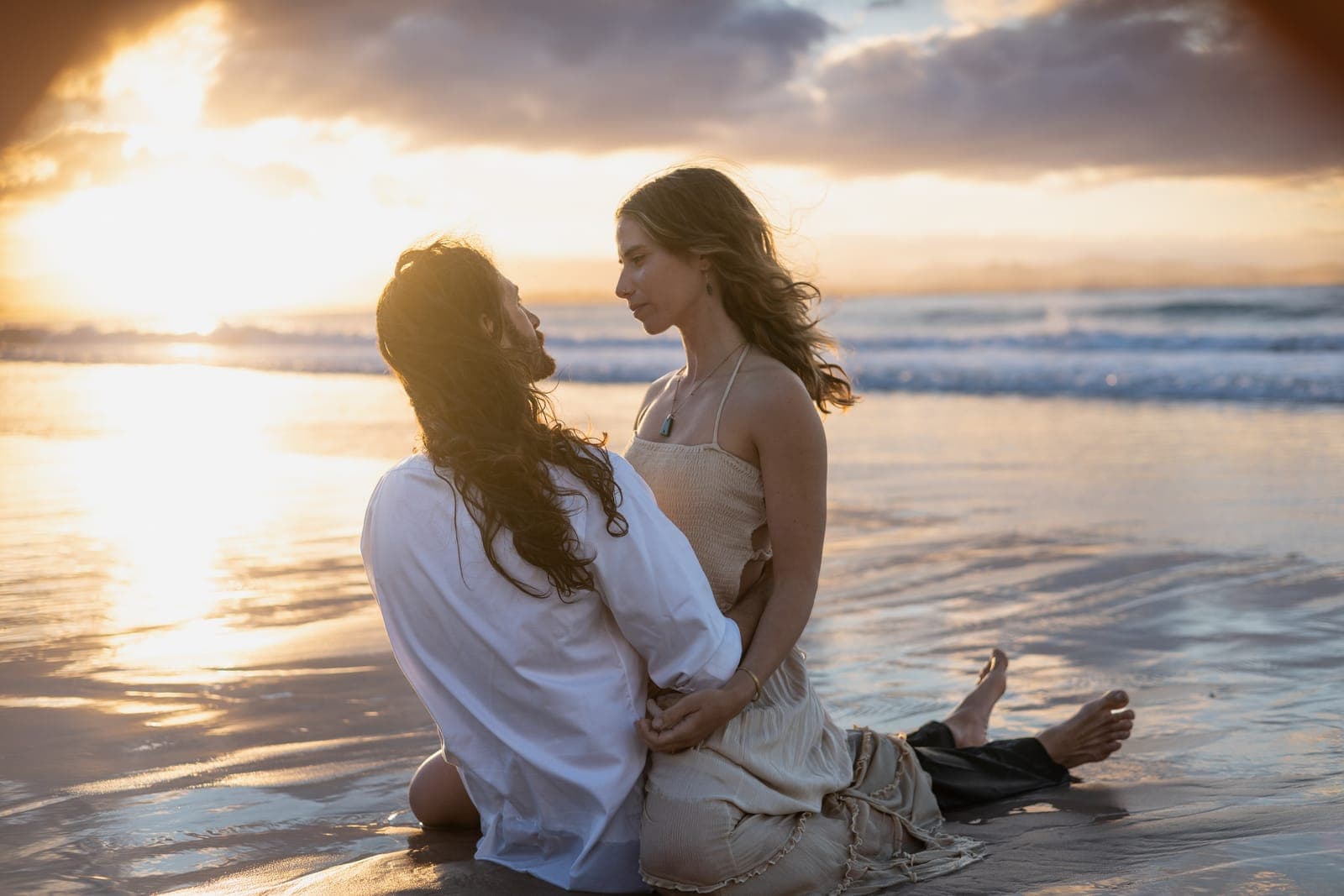 Jerome and Charlene sitting together on wet sand at sunset
