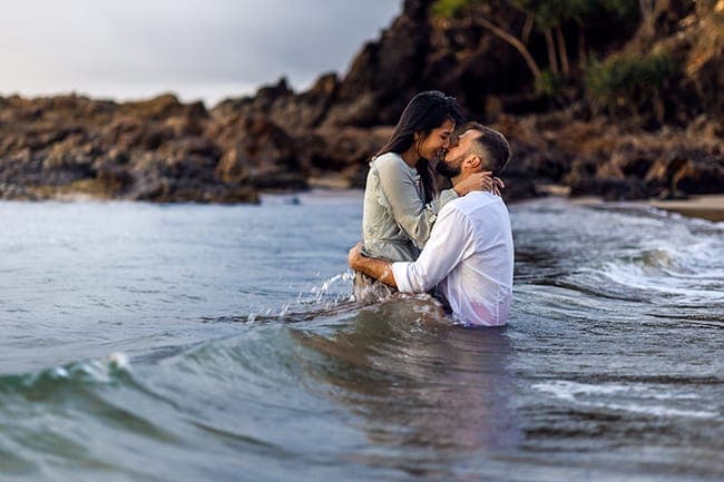 Couple kissing in the water in front of coastal rocks