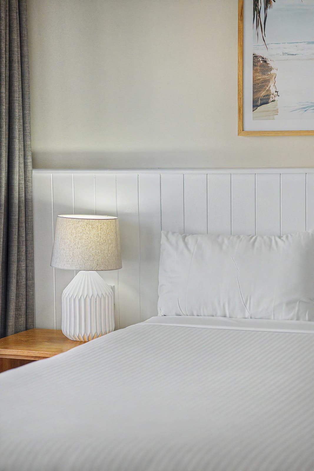 Bedside lamp glowing against white panelling beside crisp bed linen