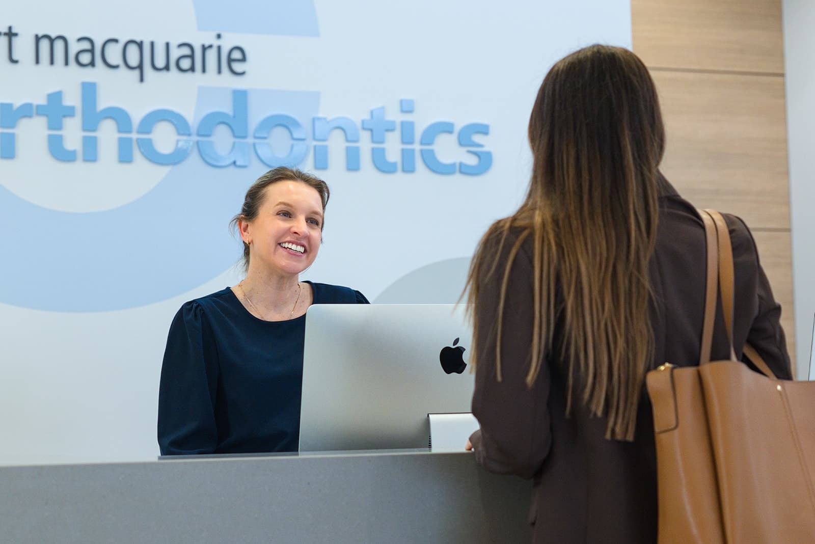 Receptionist greeting a patient beneath the orthodontics sign