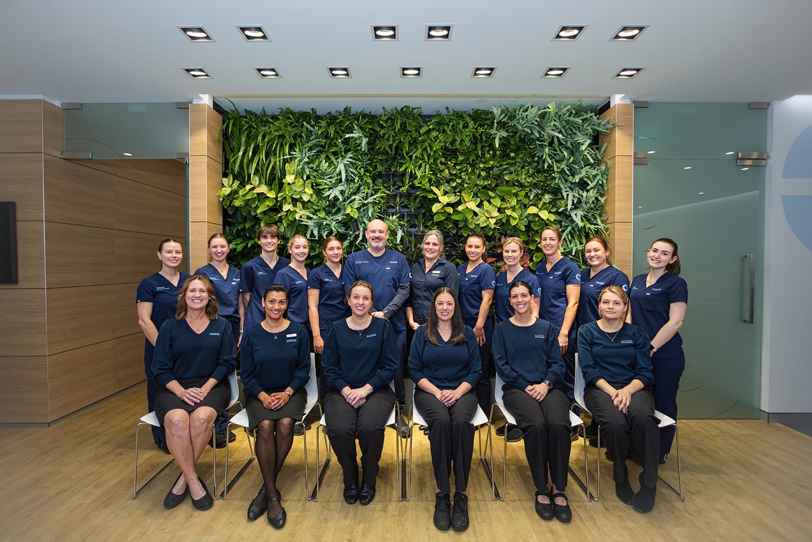 The full Port Macquarie Orthodontics team posed in front of the reception living green wall