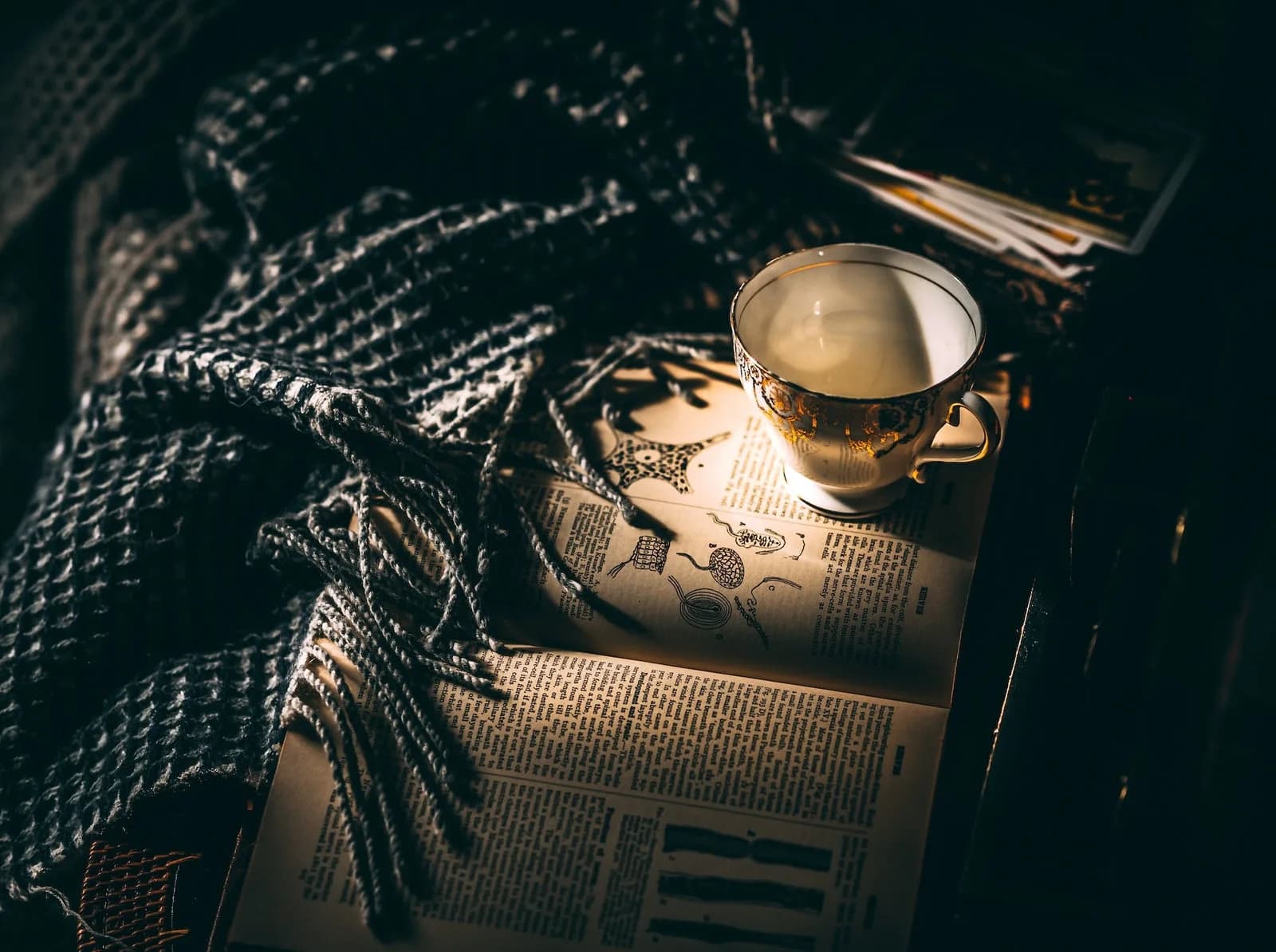 Teacup on a newspaper beside a knitted throw in moody light