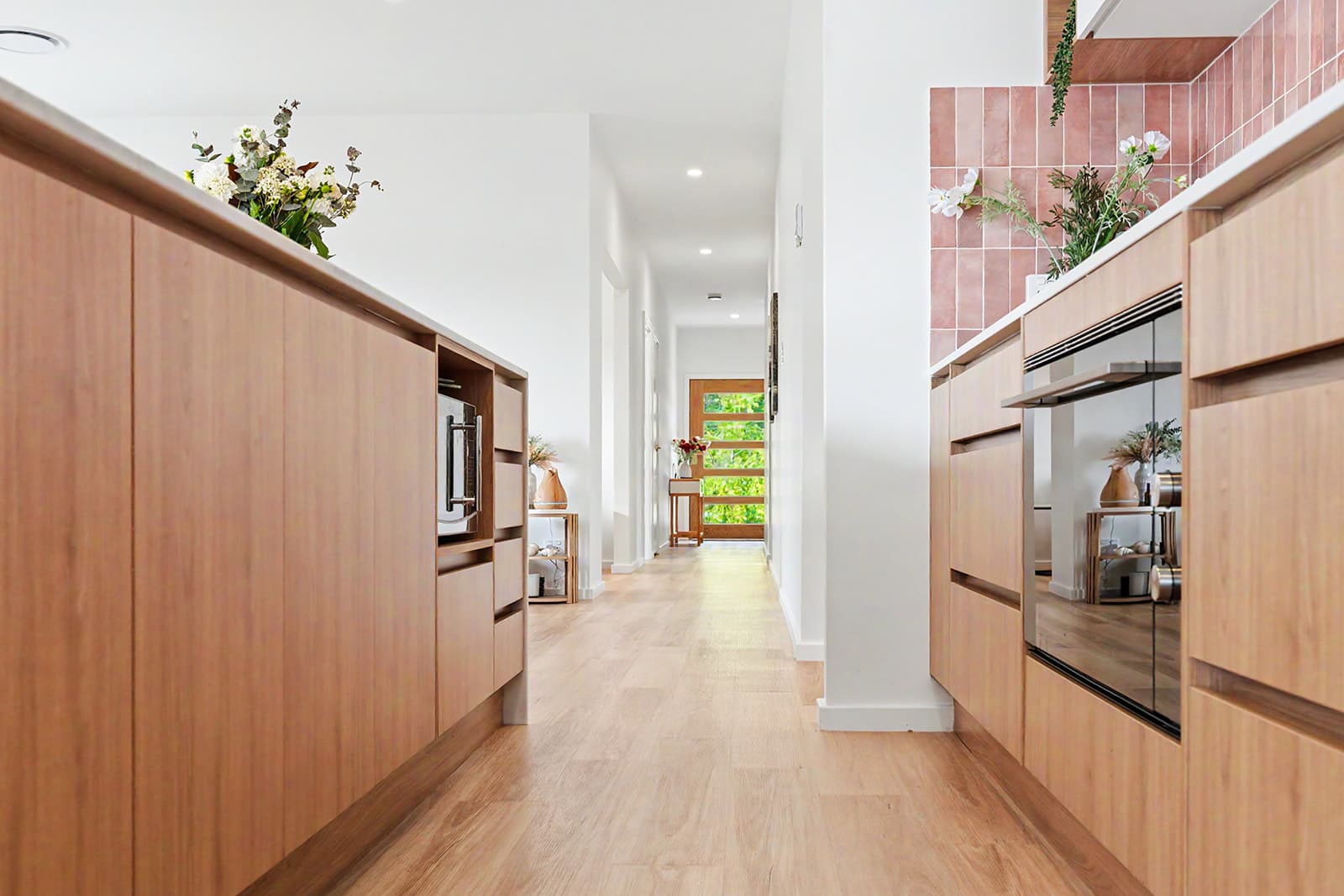 Low view between timber kitchen cabinetry down the hallway to the front door