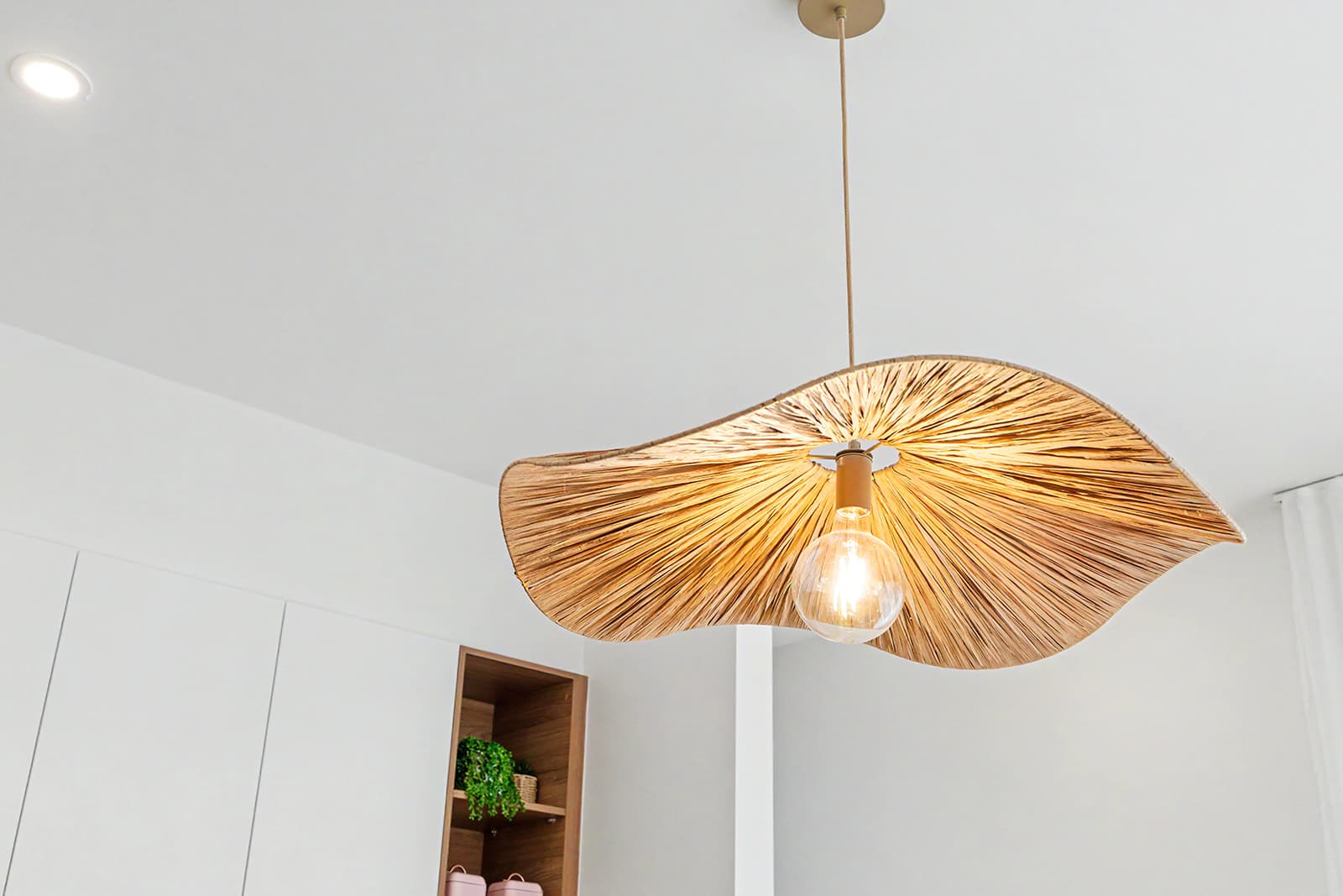 Woven rattan pendant light glowing above a white kitchen