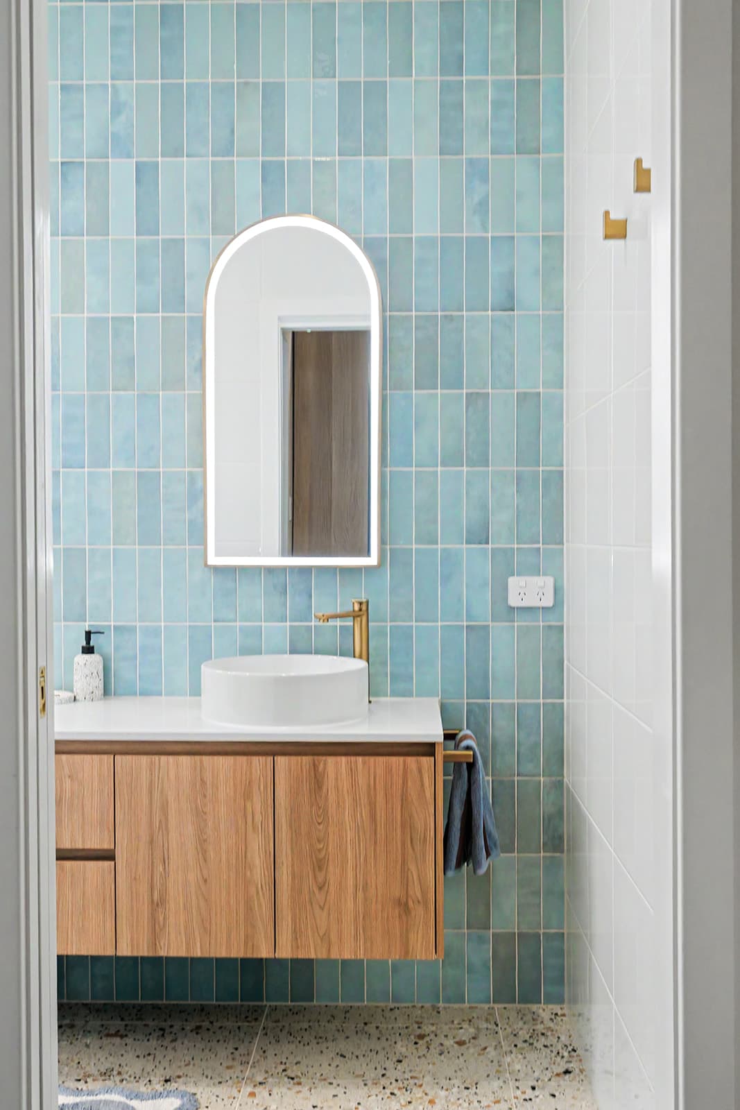 Bathroom vanity with arched mirror, blue tiles and terrazzo floor
