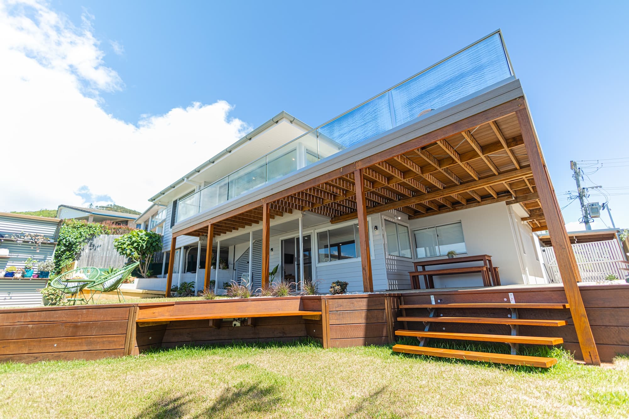Rear of a two-storey coastal home with a timber deck, glass balcony and lawn