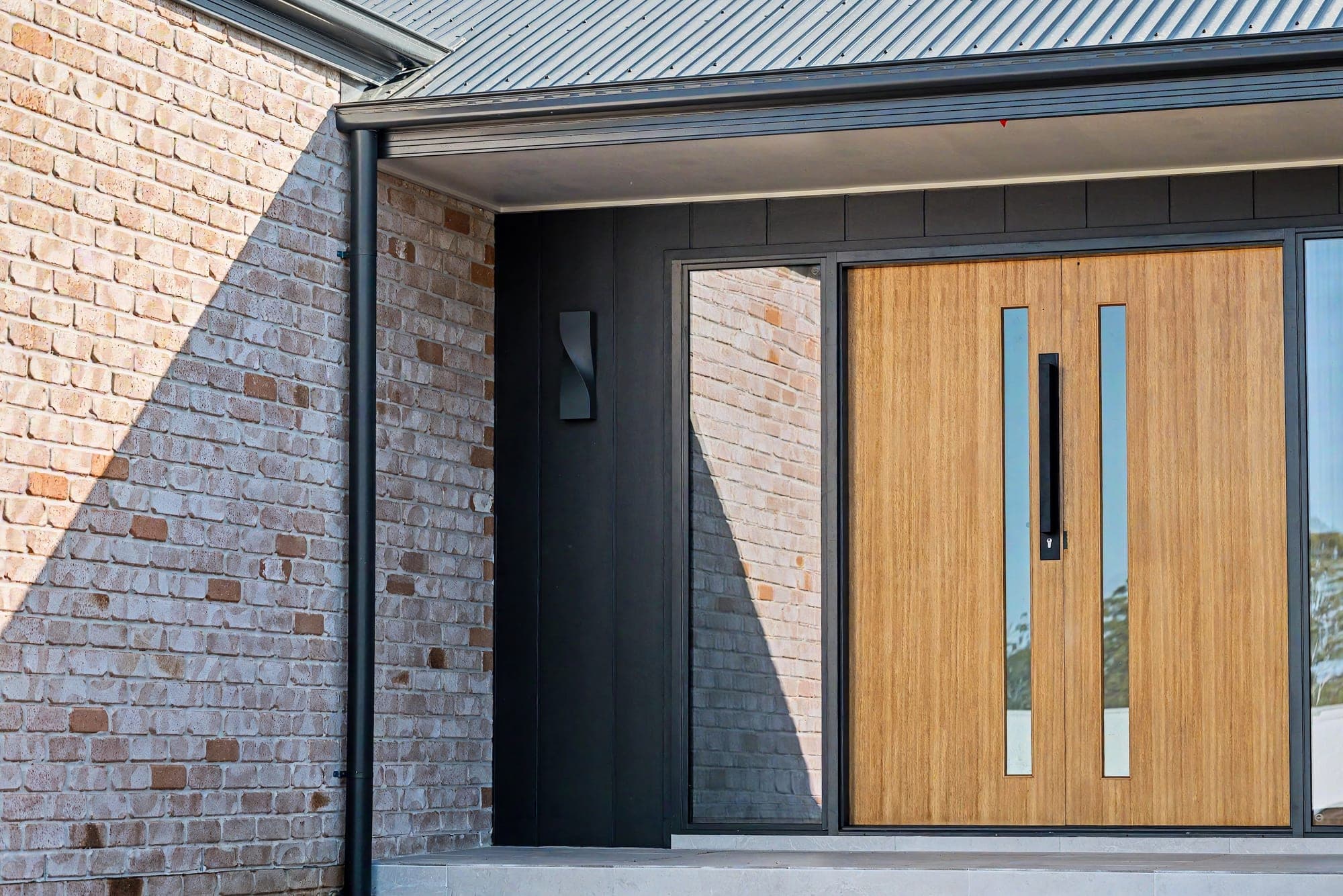 Timber double entry door framed by black cladding and recycled brick