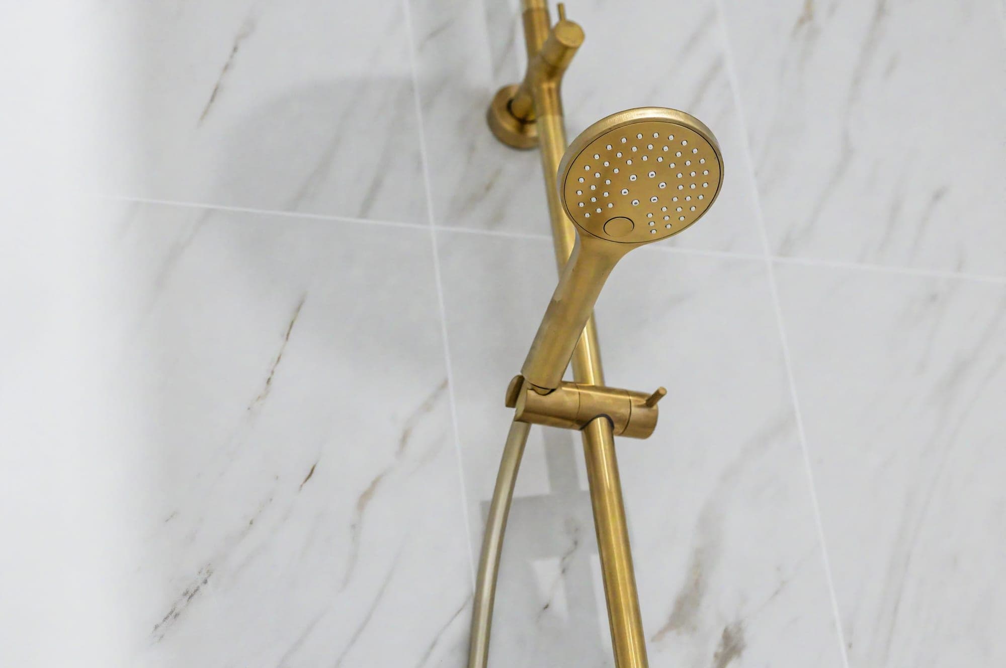 Brushed brass hand shower against marble-look tiles