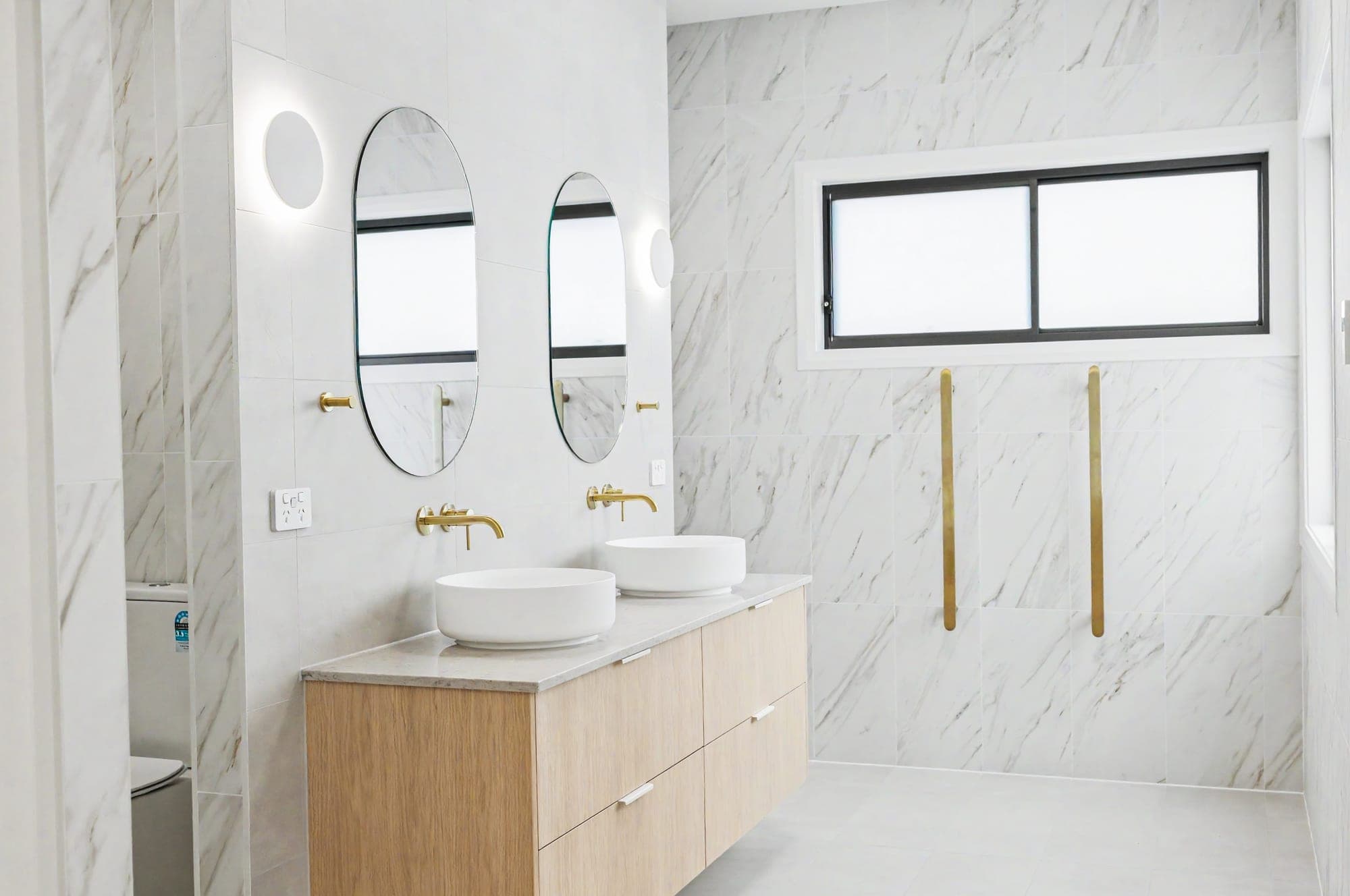 Double timber vanity with vessel basins, oval mirrors and brushed brass tapware