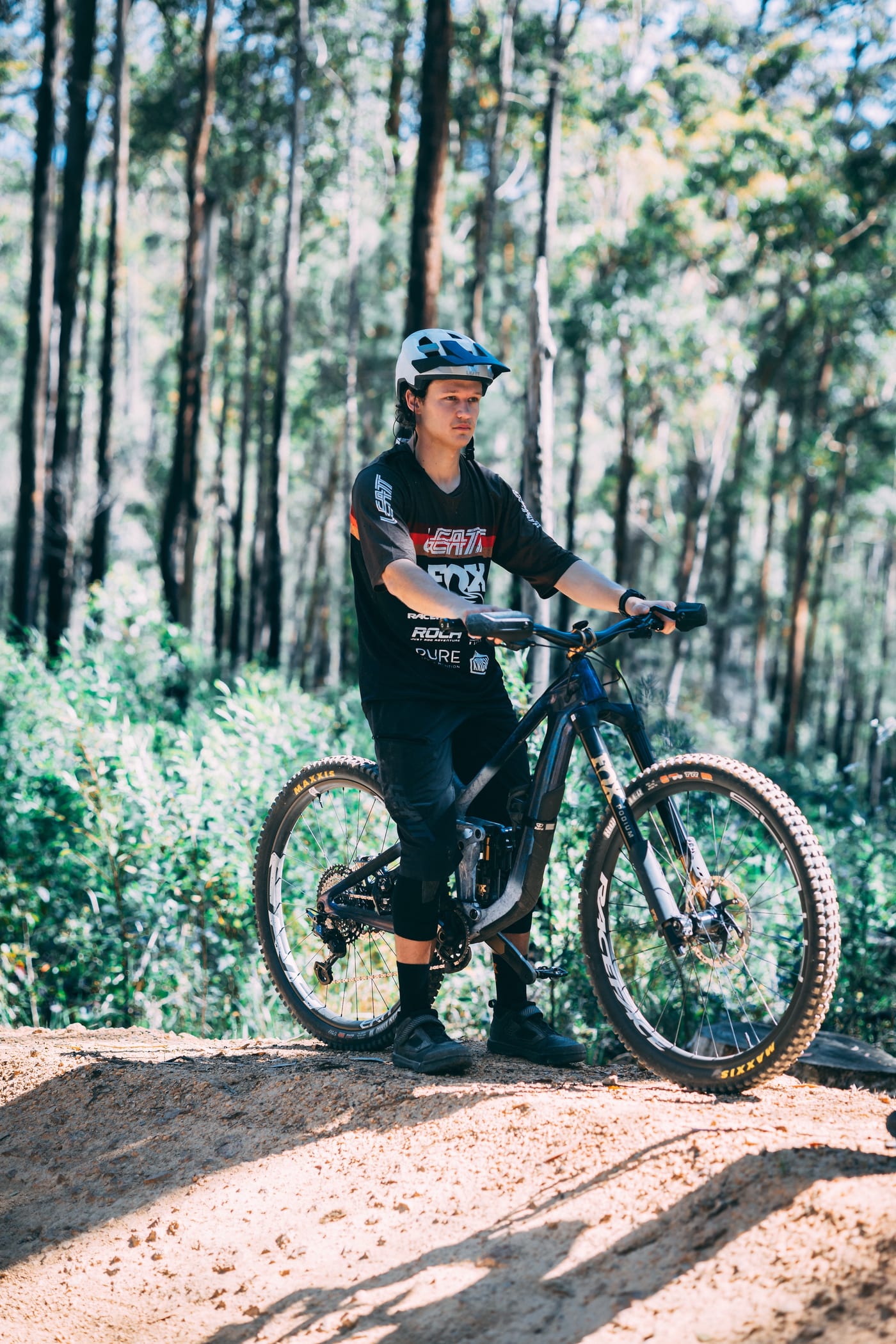 Tom Jenkins standing with his bike at the top of a dirt trail among tall gums