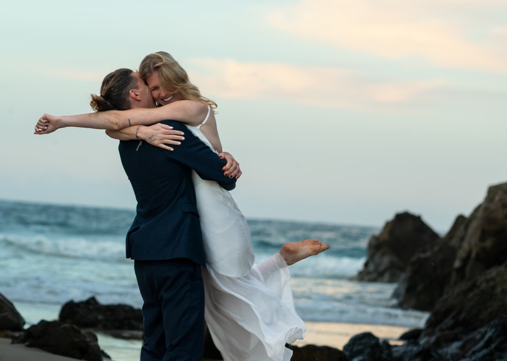 Groom lifting the bride on the sand as waves roll in