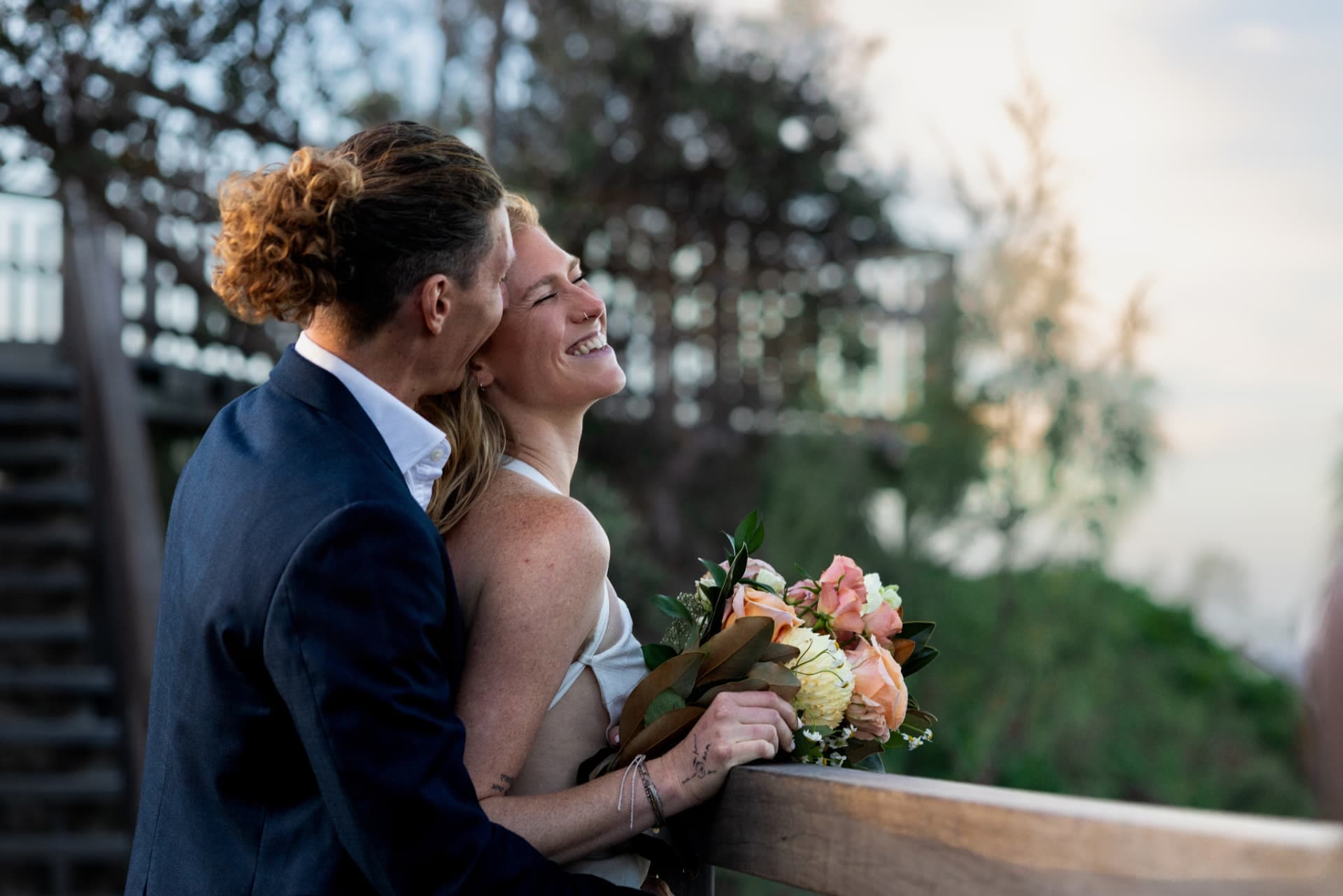 Couple embracing beside a timber rail, bride holding a native bouquet