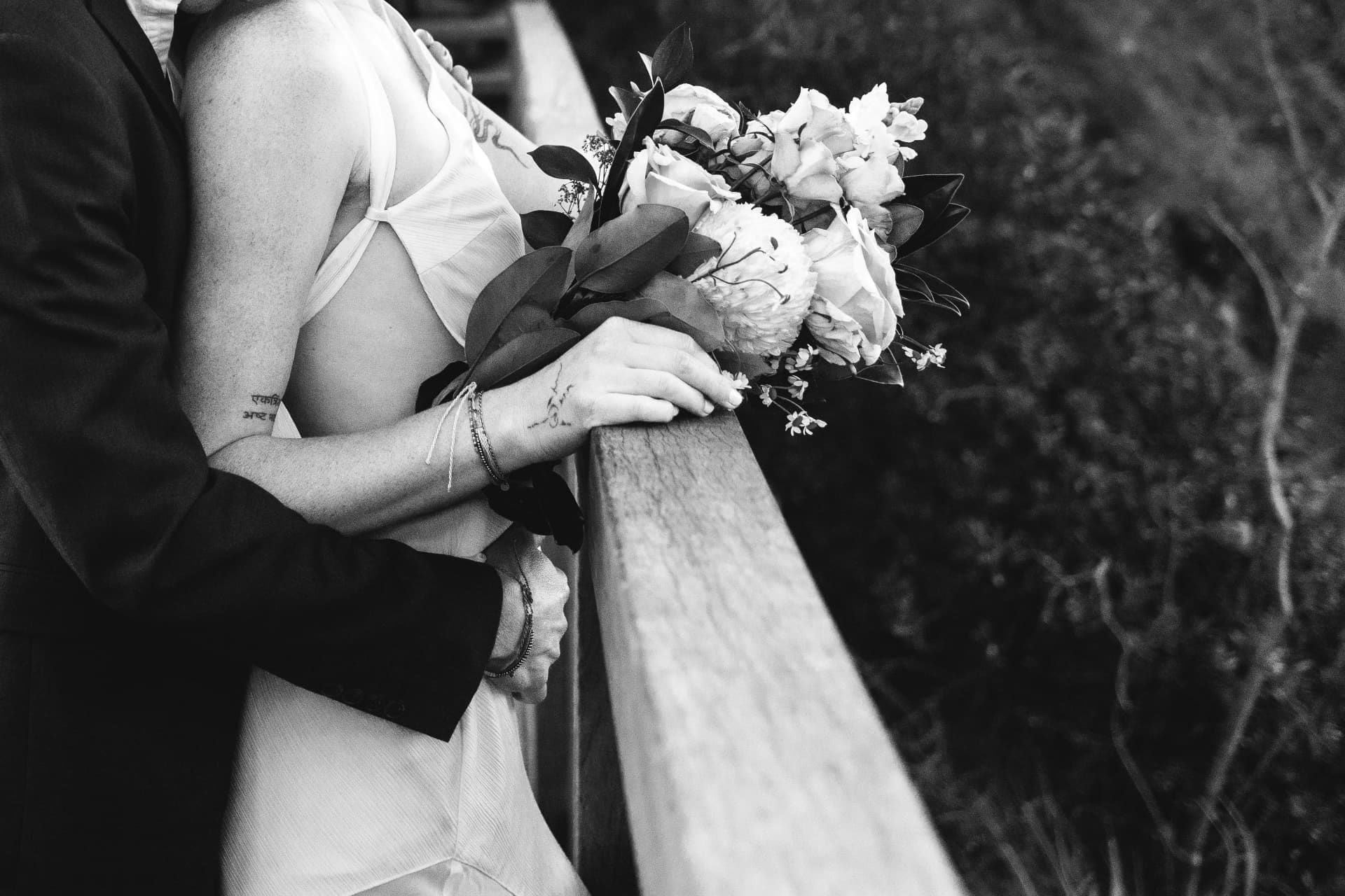 Black and white detail of the bride resting her bouquet on a timber rail